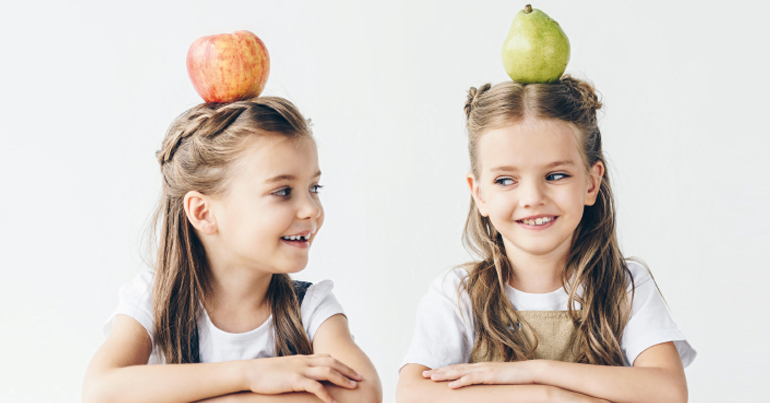 Zwei Mädchen mit einem Apfel und einer Birne auf dem Kopf