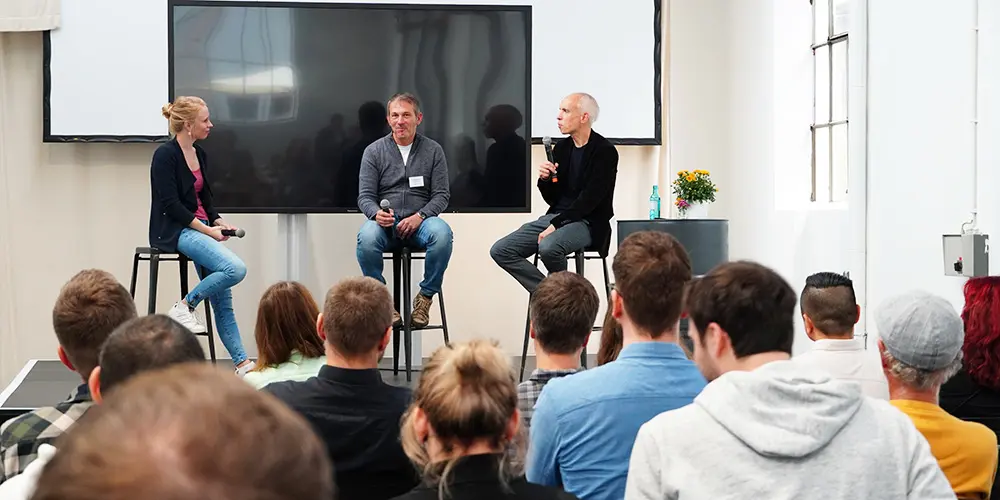 Podiumsdiskussion mit 3 Personen, die auf Barhockern sitzen